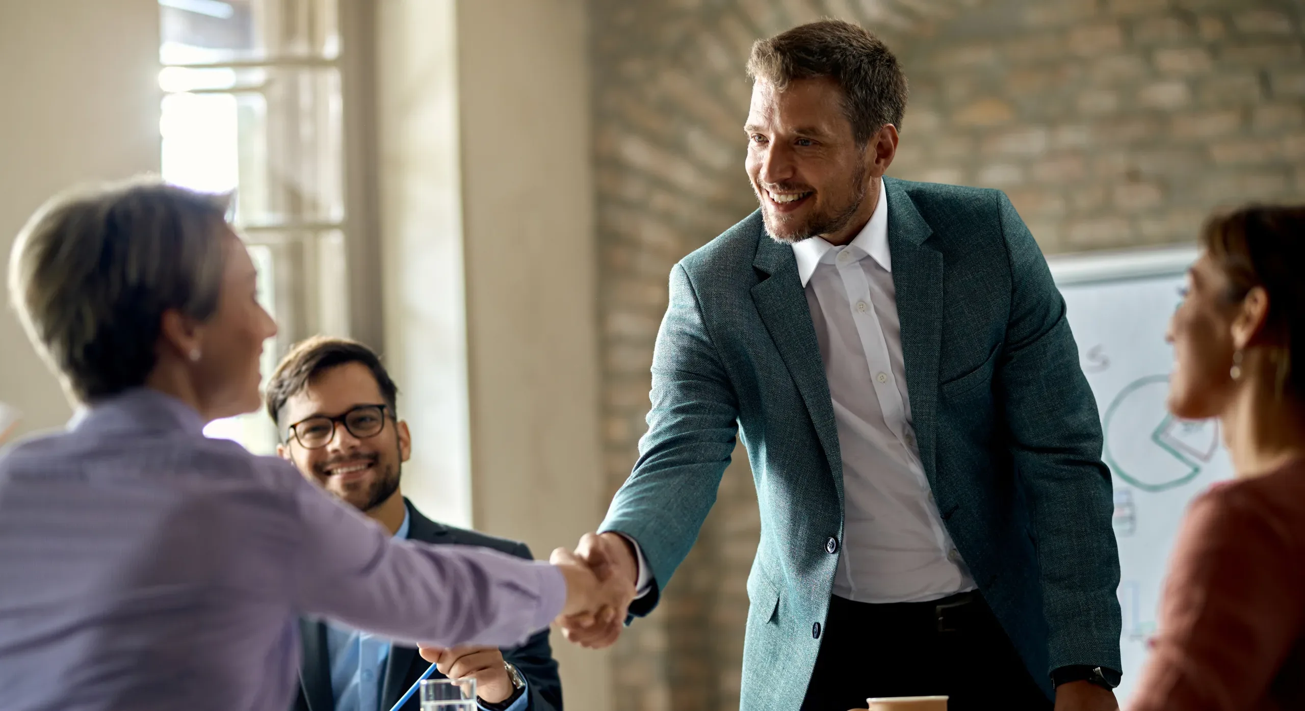 Business coworkers shaking hands during a meeting in the office. Focus is on a businessman.
